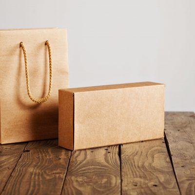 Craft paper bag and cardboard blank box presented on rustic wooden table, isolated on white background